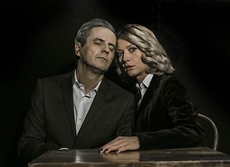 Zdjęcie przedstawia siedzących przy stole mężczyznę i kobietę, przytulonych do siebie
