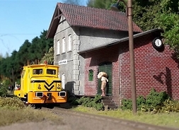 Zdjęcie przedstawia fragment makiety, na której widać zabudowania kolejowe oraz lokomotywę stojącą na torach