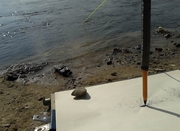 Instalacja artystyczna. Wielki ołówek i karton leżący przy brzegu rzeki