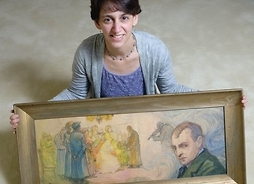Kobieta siedzi na podłodze, przed sobą trzyma obraz, na którym namalowana jest grupa osób oraz portret mężczyzny