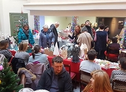 Zdjęcie przedstawia grupę osób biorących udział w kiermaszu bożonarodzeniowym odwiedzających stoiska wystawców