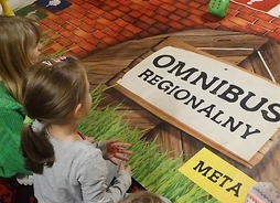 Zdjęcie przedstawia dziewczykę siedzącą tyłem do obiektywu przed nią leżą plansze z napisem Omnibus regionalny i Meta