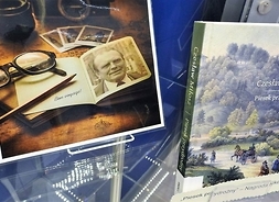Zdjęcie przedstawia fragment gabloty, w której wyeksponowane są zdjęcia pamiątek związanych z Czesławem Miłoszem oraz okładka jednej z jego książek