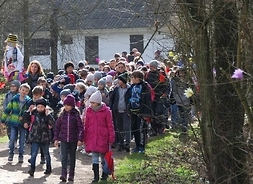 Grupa dzieci uczetniczących w idzie drogą wśród zabudowań skansenu