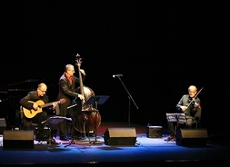 Trzej muzycy na scenie podczas występu, mężczyźni grający na instrumentach muzycznych