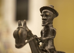 Figurka z metalu przedstawiająca jeźdźca w kapeluszu siedzącego na koniu.