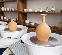 Naczynia ceramiczne ustawione na kołach garncarskich. W tle półki z ceramiką.
