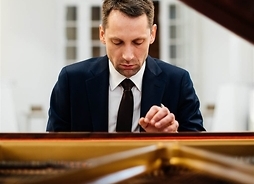 Pianista w garniturze siedzący przy fortepianie.