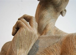 Zdjęcie przedstawia fragment rzeźby, prezentującej kobietę od szyi do pasa, z uniesioną do twarzy ręką i odsłoniętą piersią.