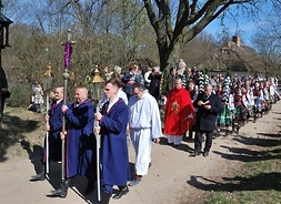 Grupa uczestników procesji Niedzieli Palmowej. Na przodzie procesji mężczyzna niosący krzyż, w asyście dwóch mężczyzn trzymających lampiony.
