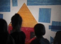 Sylwetki dzieci na tle obrazu zawierającego figury geometryczne.