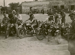 Grupa osób siedząca na motocyklach, ustawionych w półkolu na placu. Zdjęcie archiwalne.