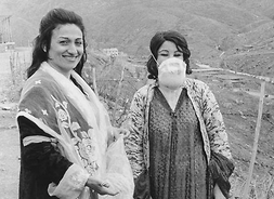 Dwie kobiety w długich sukniach, stoją na tle gór. Jedna z nich ma na twarzy maskę przeciwgazową. Zdjęcie archiwalne