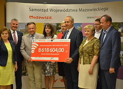 Beneficjenci i przedstawiciele zarządu województwa mazowieckiego z symbolicznym czekiem