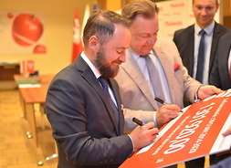 Z-ca prezydenta m. st. Warszawy Michał Olszewski podpisuje symboliczny czek