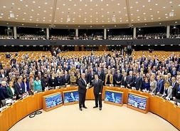 W pełnym planie sala plenarnych obrad Komitetu Regionów. Członkowie KR stoją w wielu rzędach pozując do pamiątkowego zdjęcia.