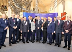 Dwudziestu członków polskiej delegacji stoi w rzędzie pozując do pamiątkowego zdjęcia.